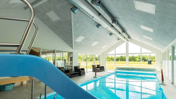An indoor swimming pool with a slide, seating area, and large windows. - 5 Star Holiday Home in Hojslev (Hojslev)