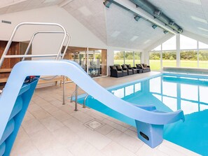 An indoor swimming pool with a slide, seating area, and a view of the outdoors. - 5 Star Holiday Home in Hojslev (Hojslev)