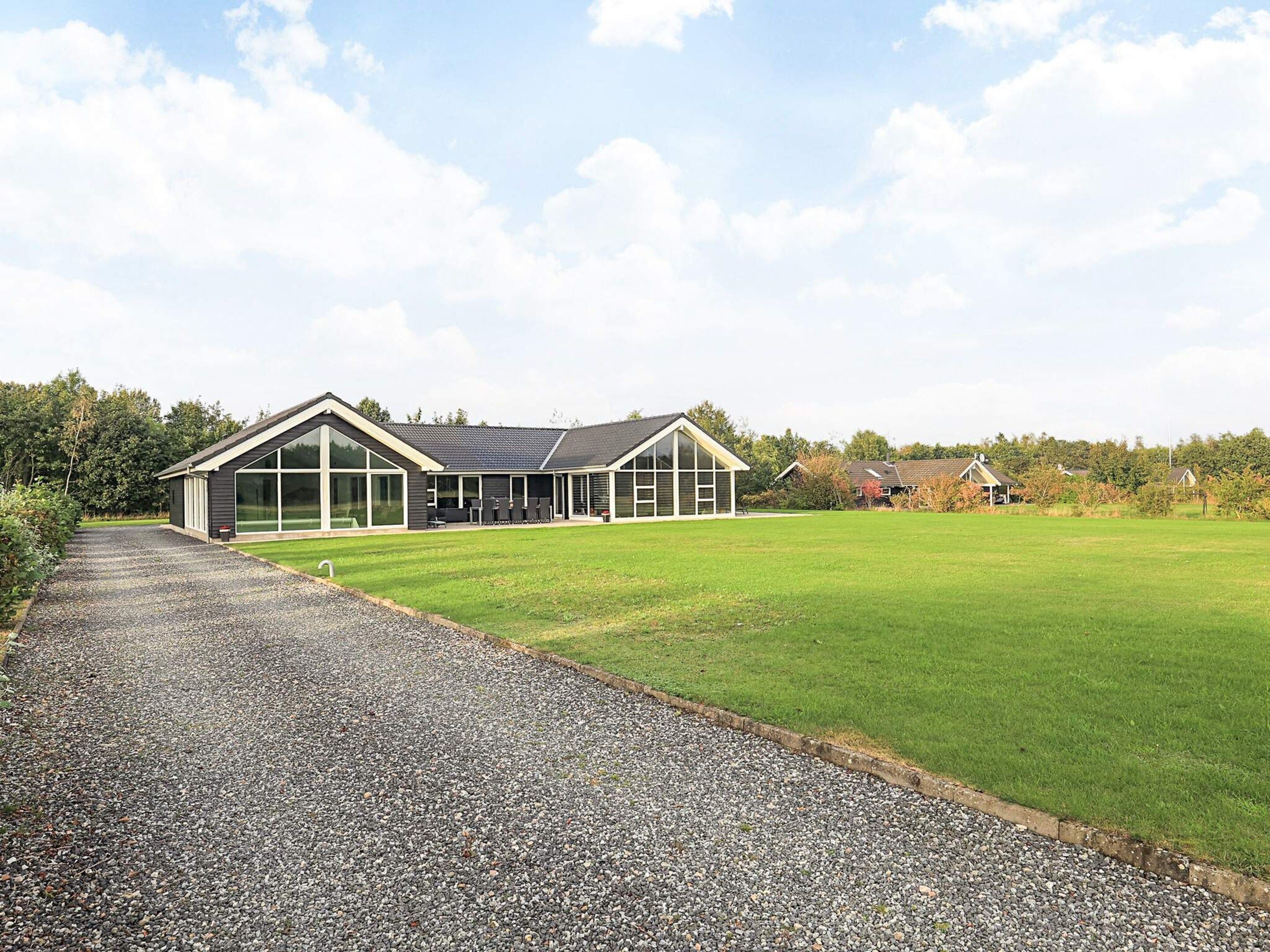 A modern building with a gravel driveway leading to a large grassy area.