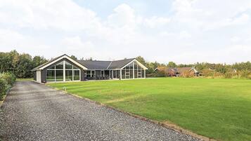 A modern building with a gravel driveway leading to a large grassy area.
