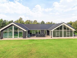 Een modern huis met grote ramen, een terras met meubilair en een verzorgd gazon.