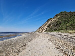 A rocky beach with a clear sky and a hill in the background. - 5 Star Holiday Home in Hojslev (Hojslev)