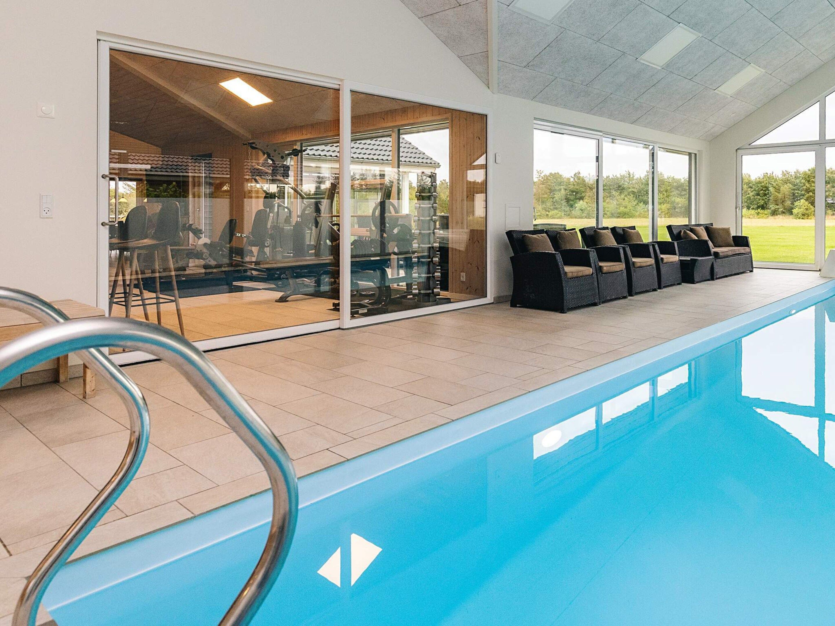Une piscine dotée d’une structure en verre, d’équipements de musculation et d’un espace de détente extérieur.