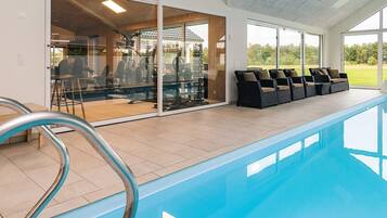 Une piscine dotée d’une structure en verre, d’équipements de musculation et d’un espace de détente extérieur.