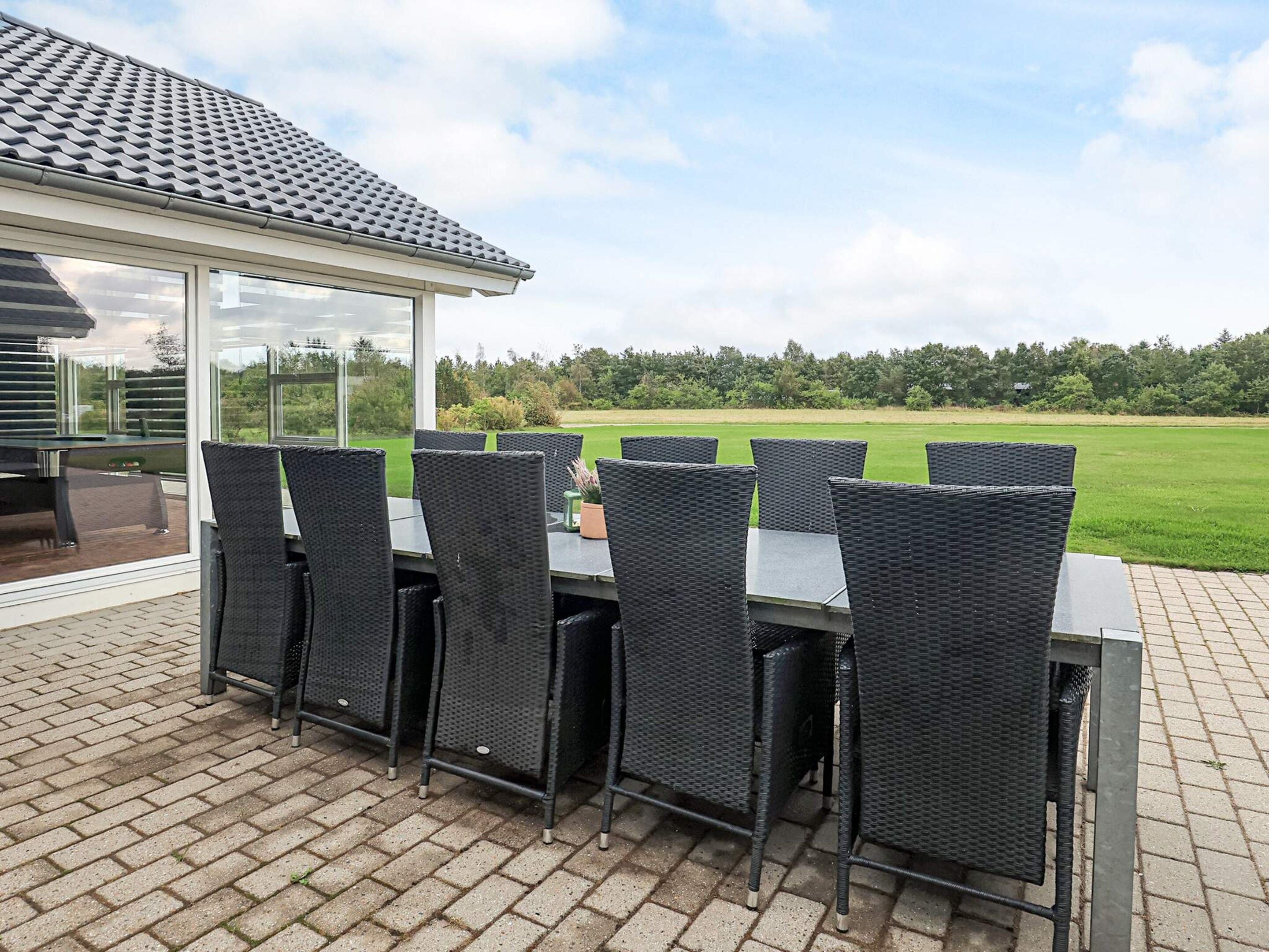 En udendørs terrasse med et bord og stole, et glasværk og udsigt over et grønt græsareal.