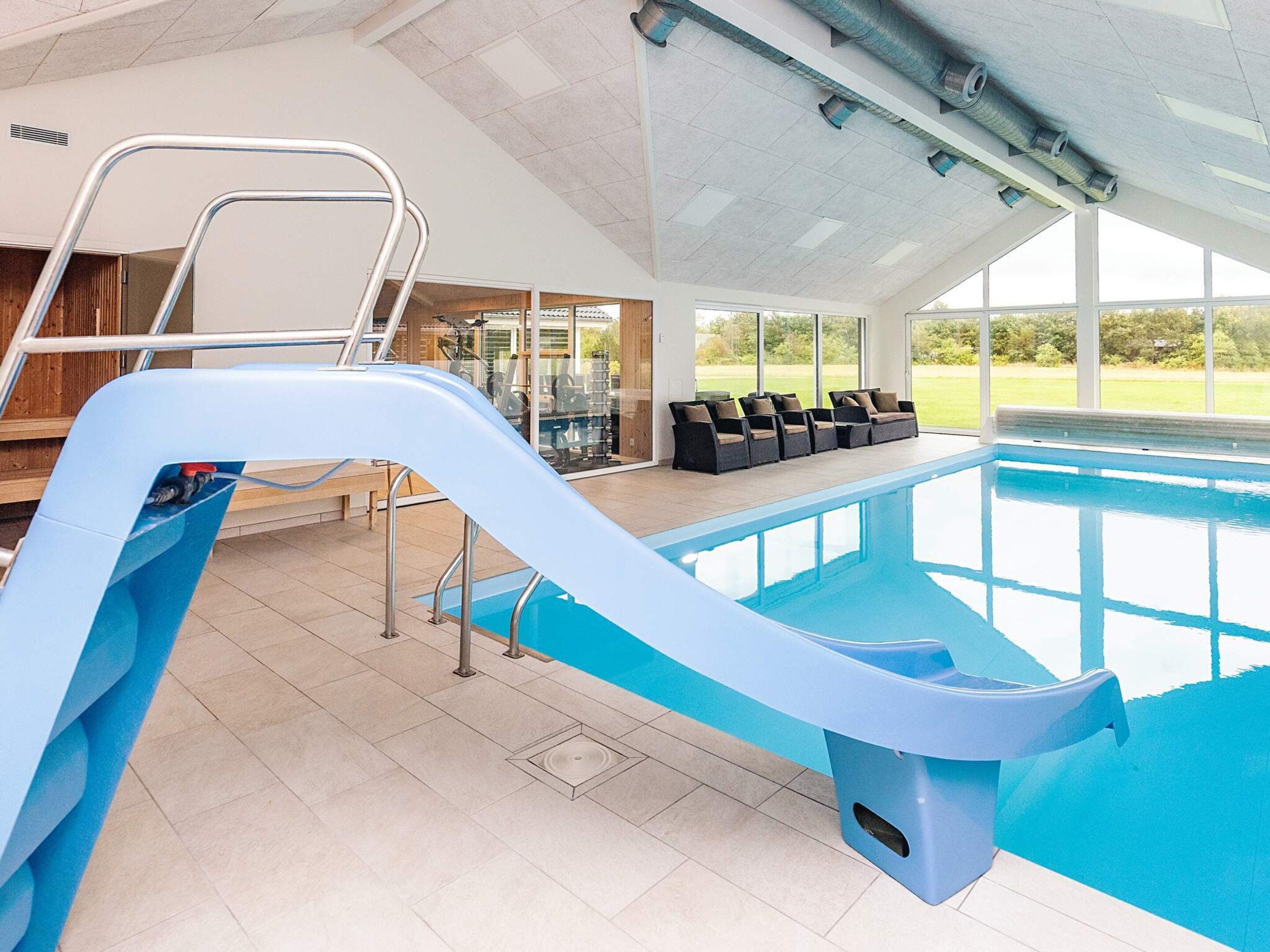 Ein Hallenbad mit Rutsche, Sitzgelegenheiten und Blick ins Freie.
