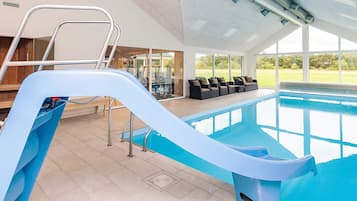 Ein Hallenbad mit Rutsche, Sitzgelegenheiten und Blick ins Freie.