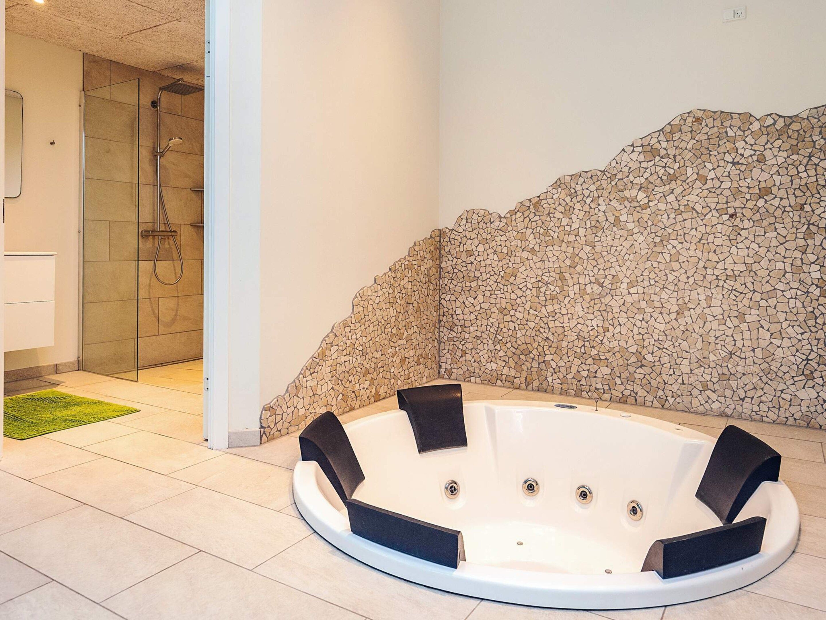 Un espace bien-être comprenant un jacuzzi, une douche en verre et un mur décoré de mosaïques.