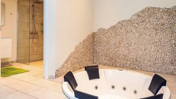Un espace bien-être comprenant un jacuzzi, une douche en verre et un mur décoré de mosaïques.