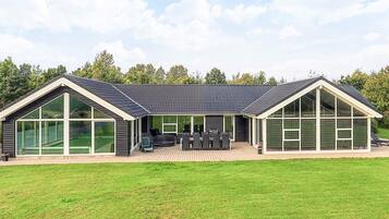Een modern huis met grote ramen, een terras met tuinmeubilair en een verzorgd gazon.