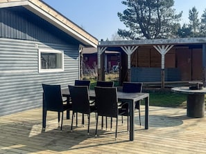 A wooden deck with a table and chairs, a pergola structure, and a view of a house with a window.