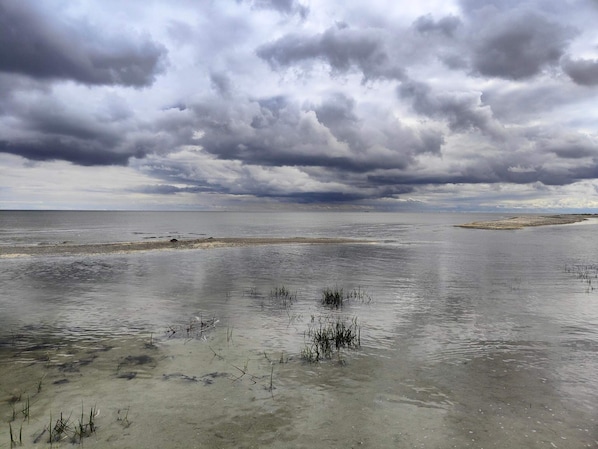 A coastal landscape with a wide expanse of water, a sandy beach, and overcast skies.
