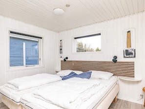 A bedroom with a bed, two windows, a bedside table, and a wall-mounted light fixture.