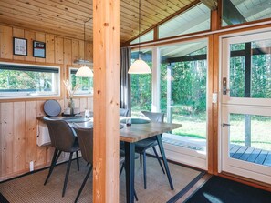 A wooden interior with a dining table, chairs, pendant lights, and large windows offering a view of greenery. - Elegant Holiday Home in Nordjylland near Sea (Læsø)