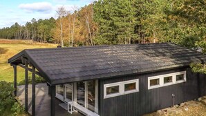 Pieni, tummanvärinen mökki, jossa on katettu kuisti ja useita ikkunoita.