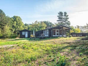 A two-story cabin with a porch, surrounded by a grassy field and trees. - Elegant Holiday Home in Nordjylland near Sea (Læsø)