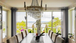 Une salle à manger avec une longue table, des chaises, un lustre et une vue sur un lac.