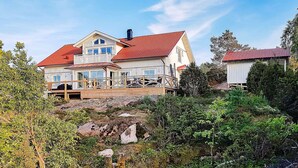 Une grande maison à deux étages, avec un toit recouvert de tuiles rouges, une terrasse en bois et un paysage rocheux.