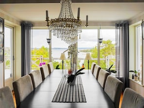 A dining area with a long table, chairs, a chandelier, and a view of the outdoors. - Holiday Home in Klövedal (Klovedal)