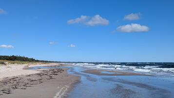 A beach with a clear sky, waves, and a person walking.
