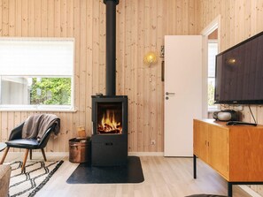 A cozy room with a wood-burning stove, a television, and a chair. - 8 Person Holiday Home in Vaeggerlose (Vaeggerlose)