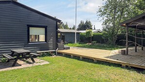 Ein modernes Haus mit dunkler Fassade, einer Holzterrasse und einem Picknicktisch.
