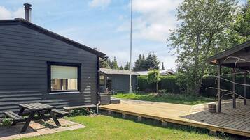 A modern house with a dark exterior, a wooden deck, and a picnic table.
