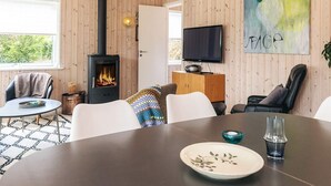 Ein gemütliches Wohnzimmer mit Holzwand, Kamin, Fernseher und einem Esstisch mit Stühlen.