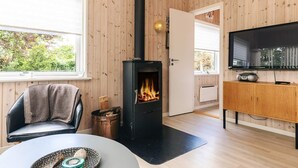 Ein gemütlicher Raum mit Holzwandverkleidung, einem schwarzen Kaminofen, einem Fernseher und einer Essecke mit Tisch und Stühlen.