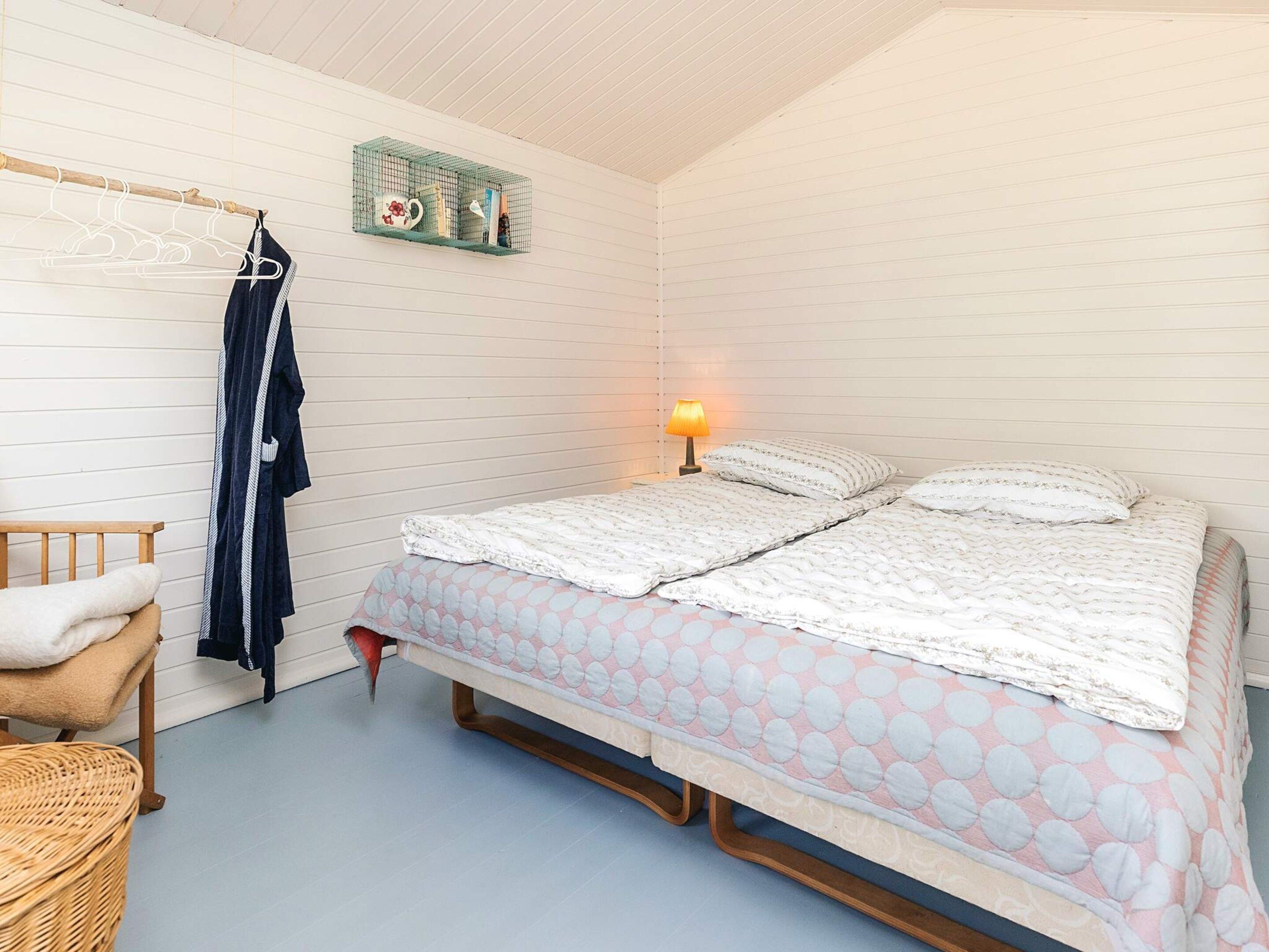 Un dormitorio con una cama, una mesita de noche, una lámpara, un perchero y una silla de mimbre.