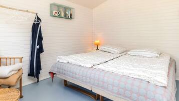 Un dormitorio con una cama, una mesita de noche, una lámpara, un perchero y una silla de mimbre.