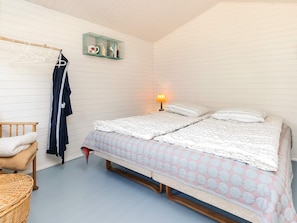 A bedroom with a bed, a bedside table, a lamp, a hanging rack, and a wicker chair. - 8 Person Holiday Home in Vaeggerlose (Vaeggerlose)