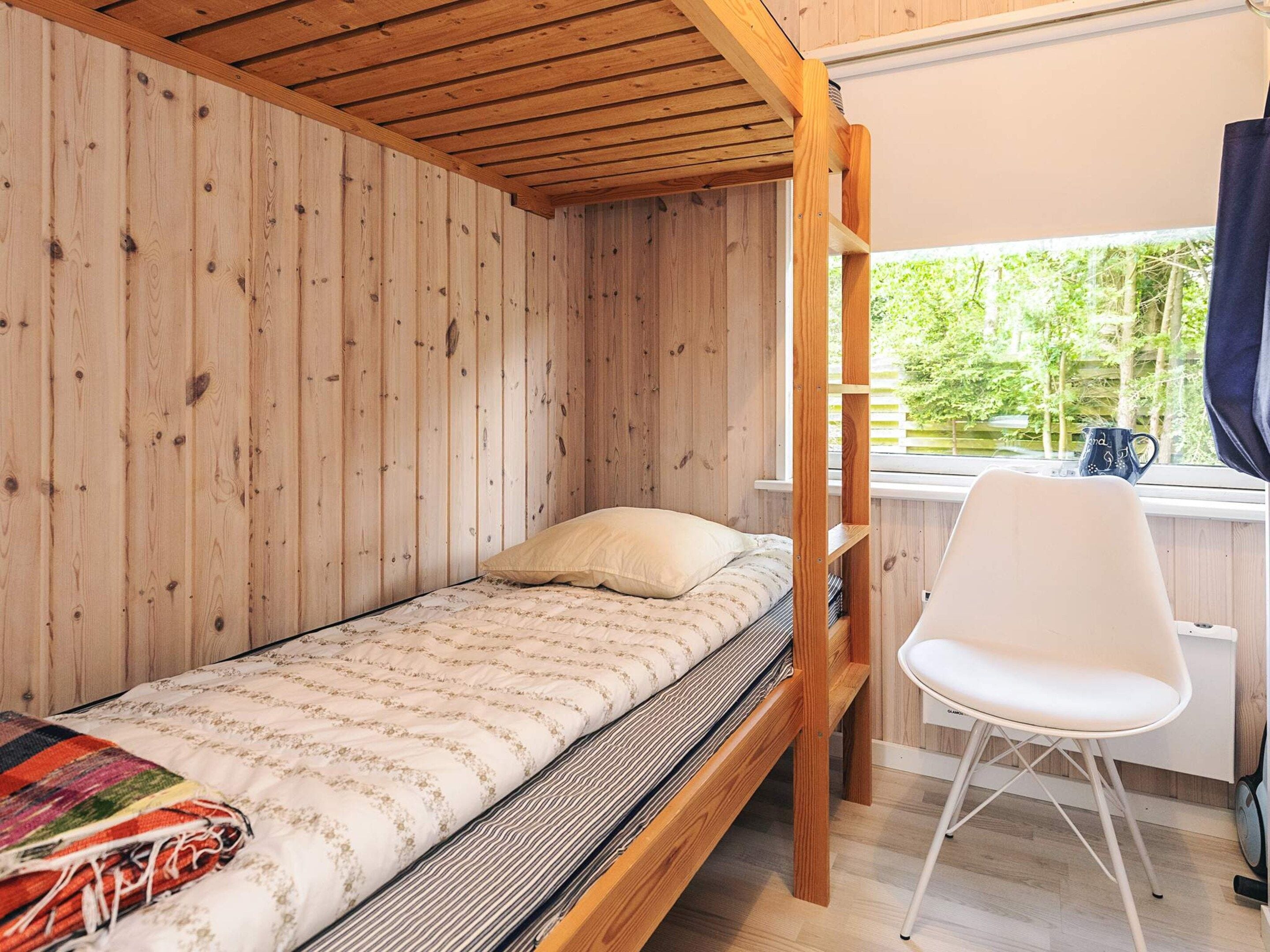 Une chambre avec un lit simple et un lit superposé en bois, une chaise blanche et une fenêtre donnant sur un paysage verdoyant.