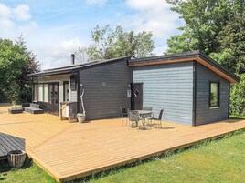 En moderne hytte med terrasse, udendørs møbler og stort vindue med udsigt over haven.