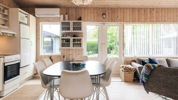 Una cocina moderna con electrodomésticos blancos, una mesa de comedor con sillas y una sala de estar acogedora con sofá y cojines.