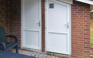 A building with two white doors, a brick wall, and a green chair outside. - 8 Person Holiday Home in Blavand (Blavand)