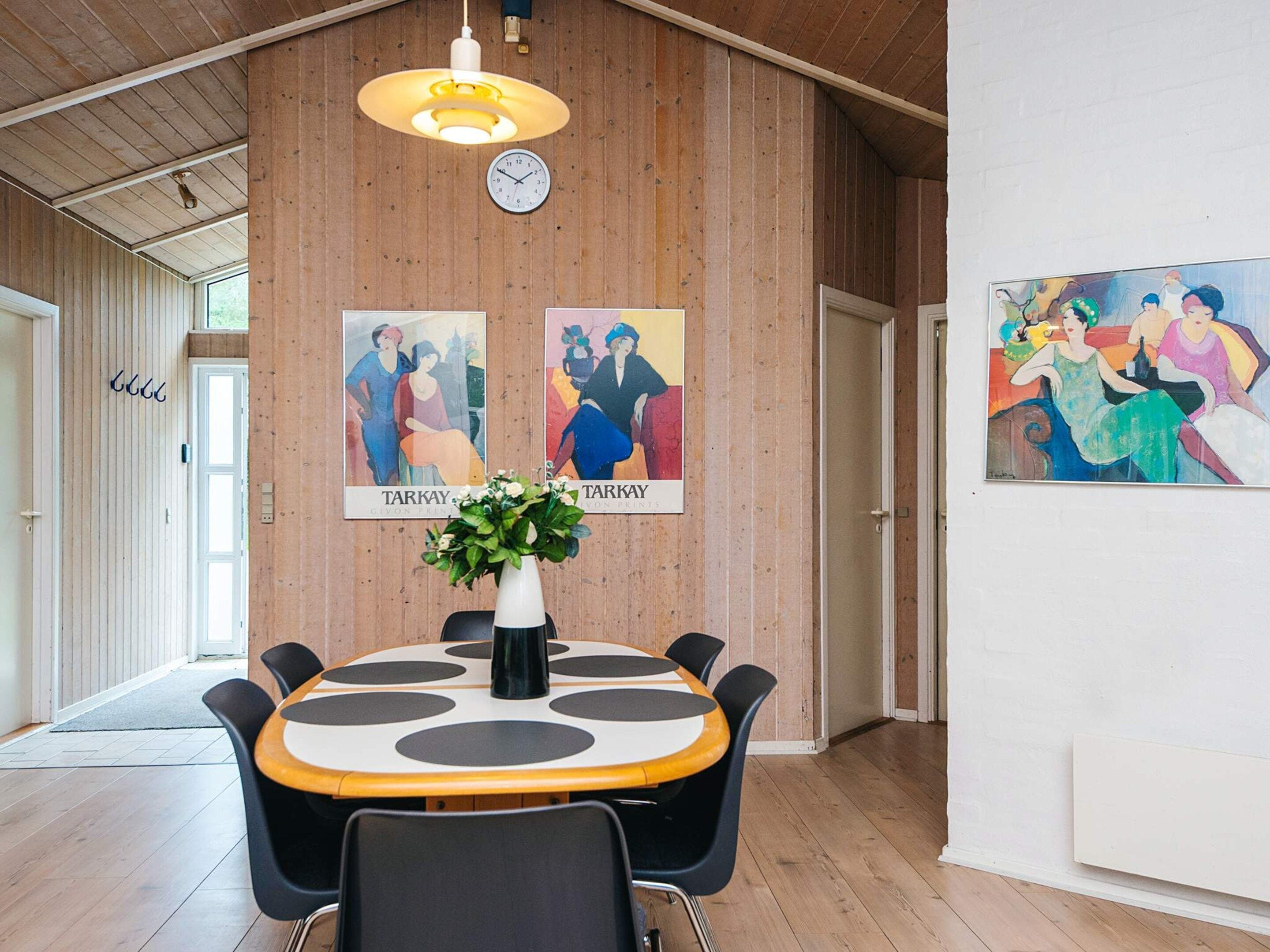 A dining area with a round table, chairs, a clock, and two framed artworks on the wall.