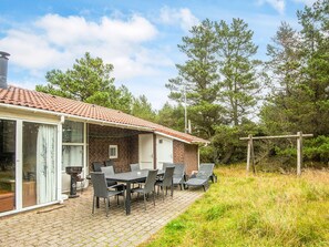 A brick house with a tiled roof, a patio with a table and chairs, and a garden area with trees and a swing. - 8 Person Holiday Home in Blavand (Blavand)