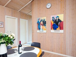A conference room with a wooden wall, two framed artworks, a clock, a table with a wine bottle, and a vase with flowers. - 8 Person Holiday Home in Blavand (Blavand)
