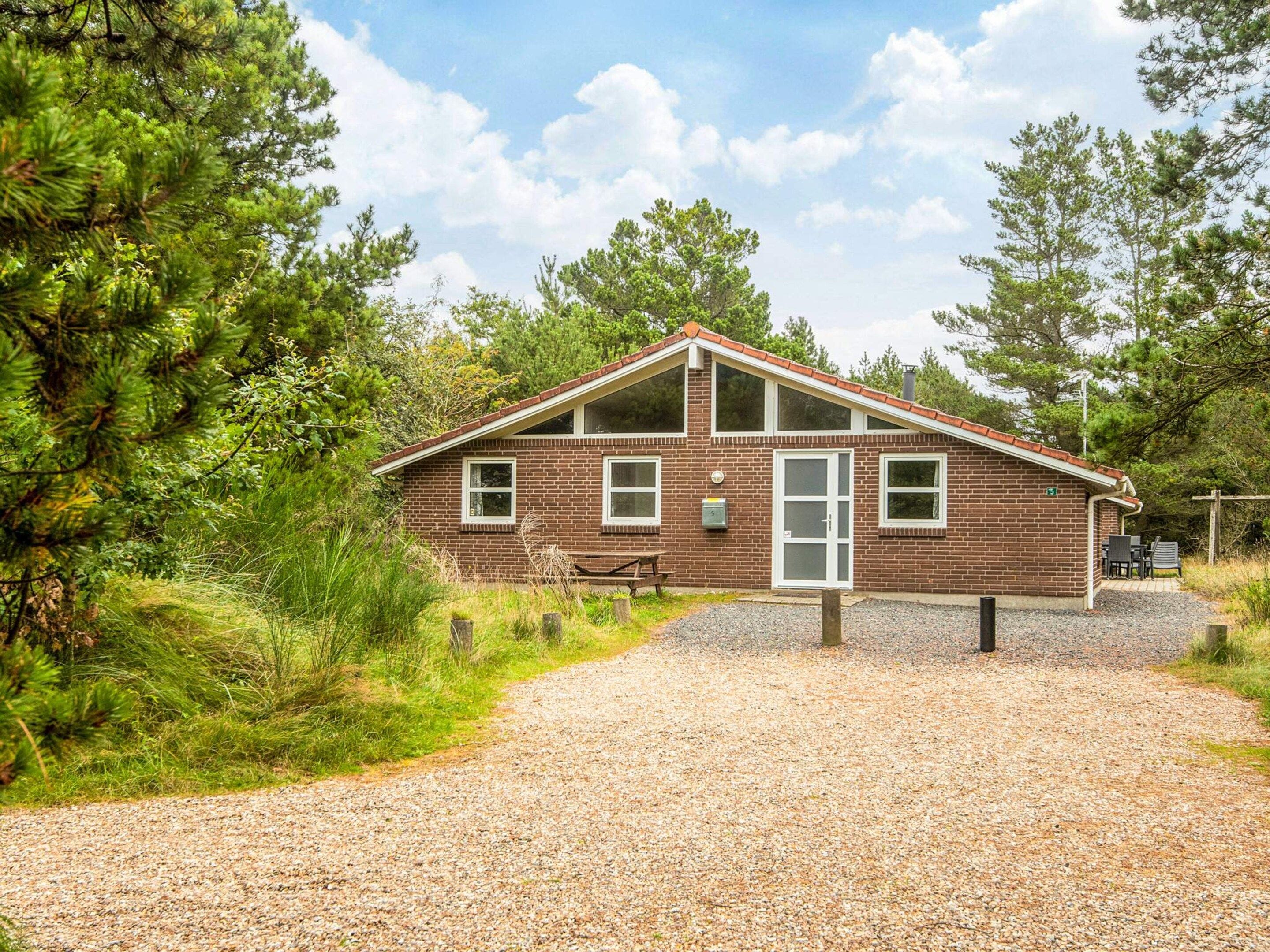 A small brick building with a gravel driveway, surrounded by trees and greenery.