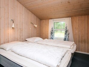 A room with two beds, wooden walls, a window with curtains, and a wall-mounted lamp. - 8 Person Holiday Home in Blavand (Blavand)