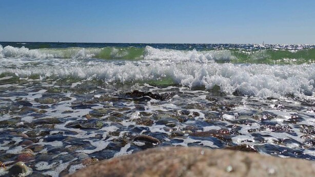 A beach with waves crashing onto rocks and a clear blue sky.