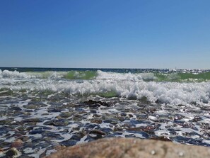 Ein Strand mit brechenden Wellen an den Felsen und blauem, wolkenlosem Himmel.
