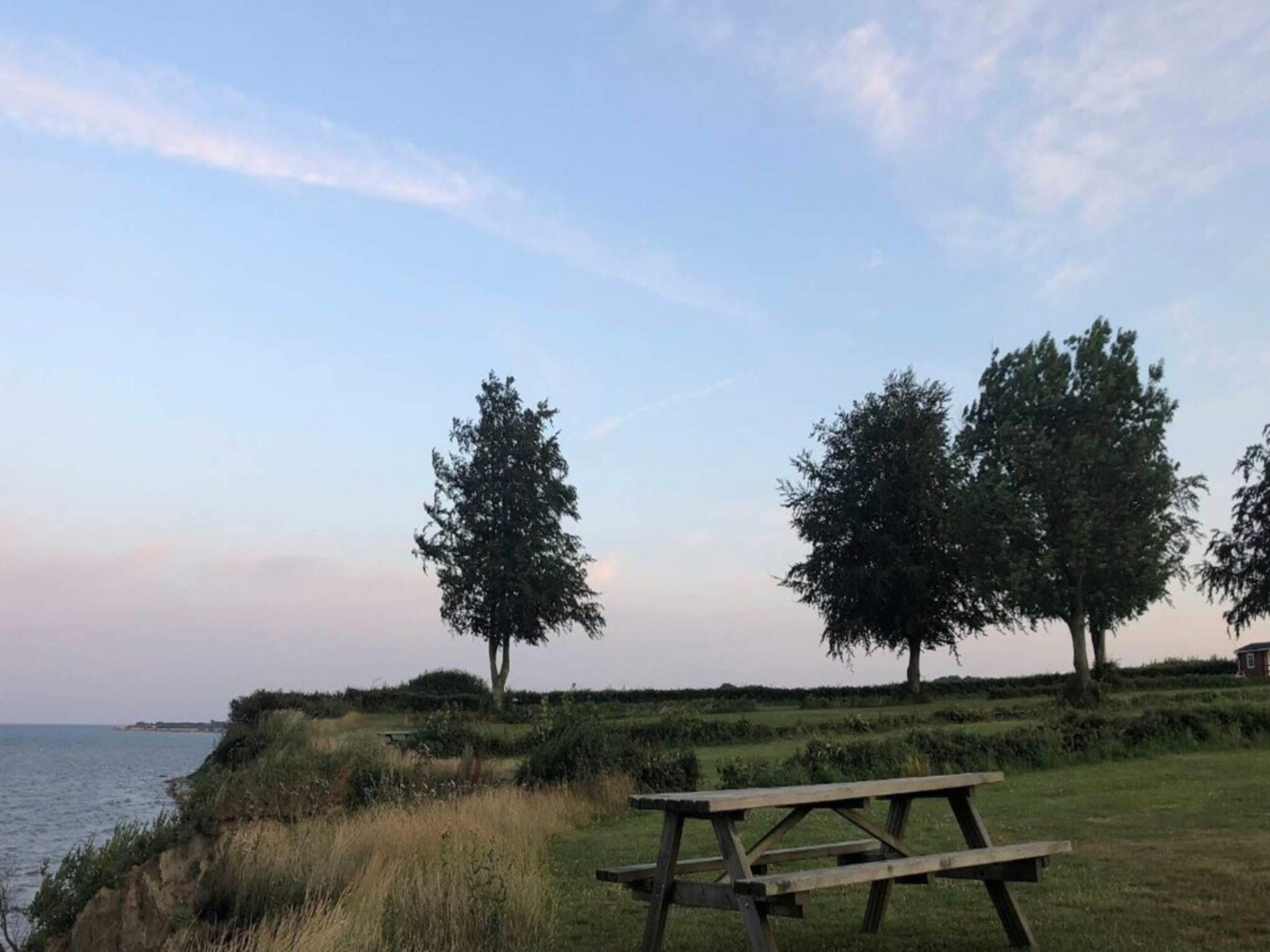 Een picknicktafel op een grasheuvel met uitzicht op een wateroppervlak.