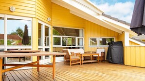 A wooden deck with a table and chairs, large windows, and a covered area.