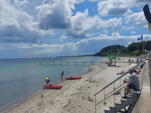 A beach with kayaks, a pier, and people relaxing.