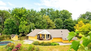 A yellow house with a porch, a small shed, and a trampoline in a green, wooded area.