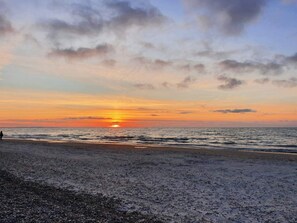 A beach with a sunset, calm sea, and a person walking.