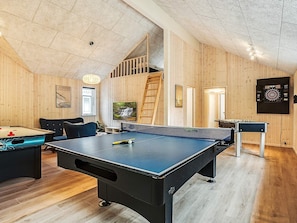 A room with a ping pong table, foosball table, dartboard, and a TV.