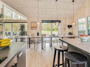 A modern kitchen with a large island, clear chairs, and a view of the outdoors.